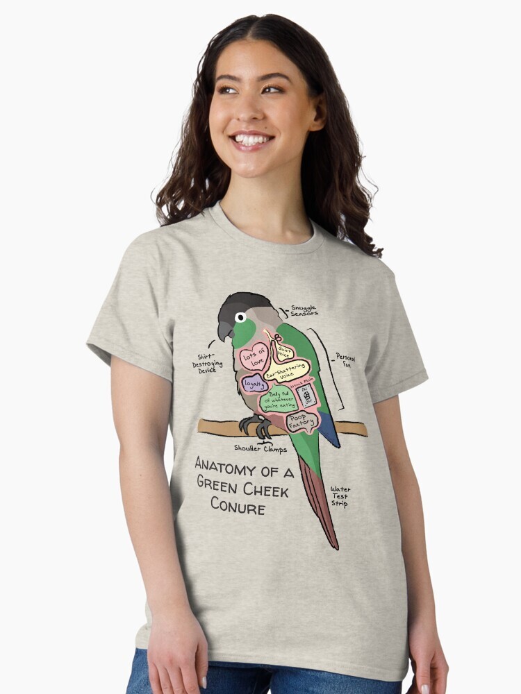 A brunette woman wearing a t-shirt  featuring a cartoon illustration titled “Anatomy of a Green Cheek Conure” showing a cute Green Cheek Conure bird with funny labeled anatomy sections.