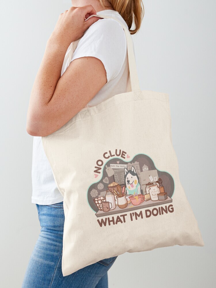 A woman wearing a white short sleeve t-shirt with a cotton tote bag on her shoulder. The tote bag features a cartoon illustration with text saying 