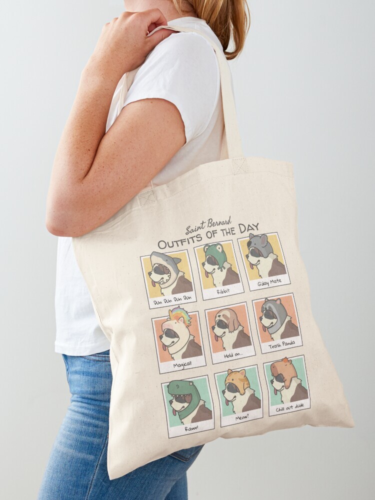 A woman wearing a white short sleeve t-shirt with a cotton tote bag on her shoulder. The tote bag features a cartoon illustration titled “Saint Bernard Outfits of the Day” showing a cute Saint Bernard dog wearing different animal hats that include: shark, frot, koala, unicorn, sloth, raccoon, dinosaur, cat and capybara with an orange