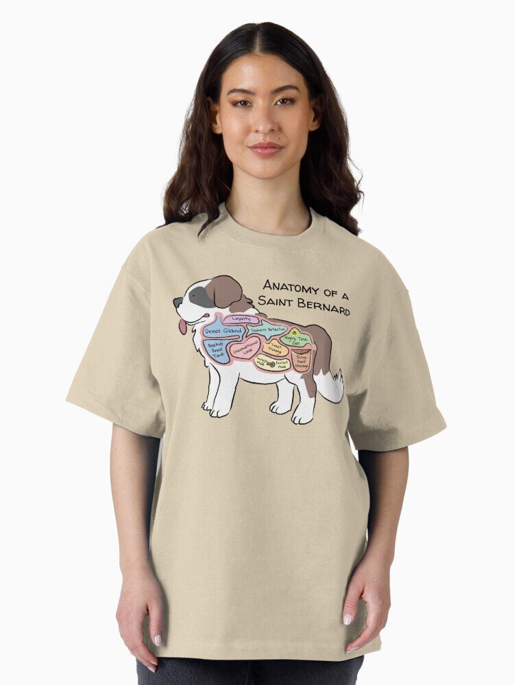 A brunette woman wearing a shirt  featuring a cartoon illustration titled “Anatomy of a Saint Bernard,” showing a cute Saint Bernard dog with funny labeled anatomy sections.