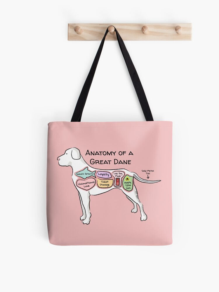 A pink-colored tote bag hanging off a wooden hook. On the tote bag features a cartoon illustration titled “Anatomy of a Great Dane” showing a cute Great Dane dog with funny labeled anatomy sections.
