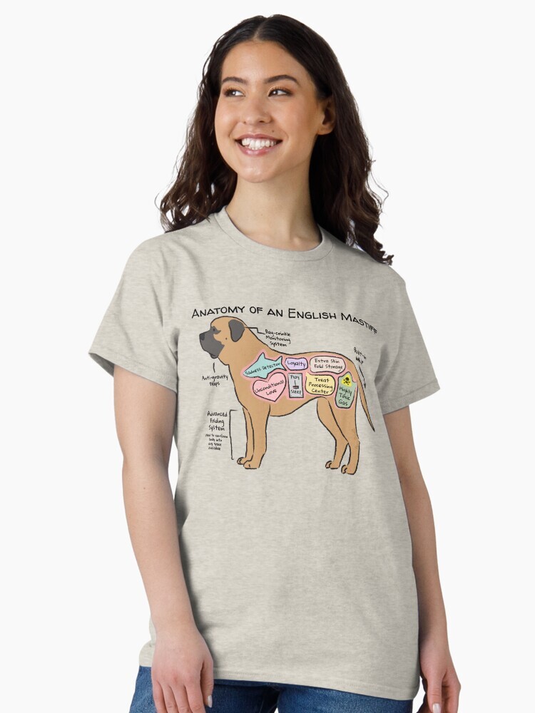 A brunette woman wearing a t-shirt  featuring a cartoon illustration titled “Anatomy of an English Mastiff” showing a cute English Mastiff dog with funny labeled anatomy sections.
