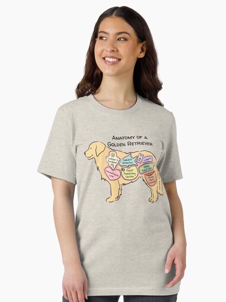 A brunette woman wearing an oversized beige t-shirt  featuring a cartoon illustration titled “Anatomy of a Golden Retriever” showing a cute Golden Retriever dog with funny labeled anatomy sections.