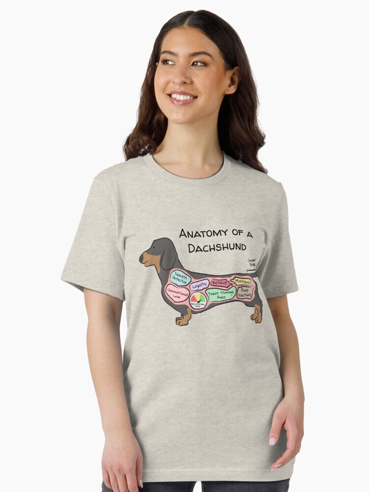 A brunette woman wearing a t-shirt  featuring a cartoon illustration titled “Anatomy of a Dachshund” showing a cute Dachshund dog with funny labeled anatomy sections.