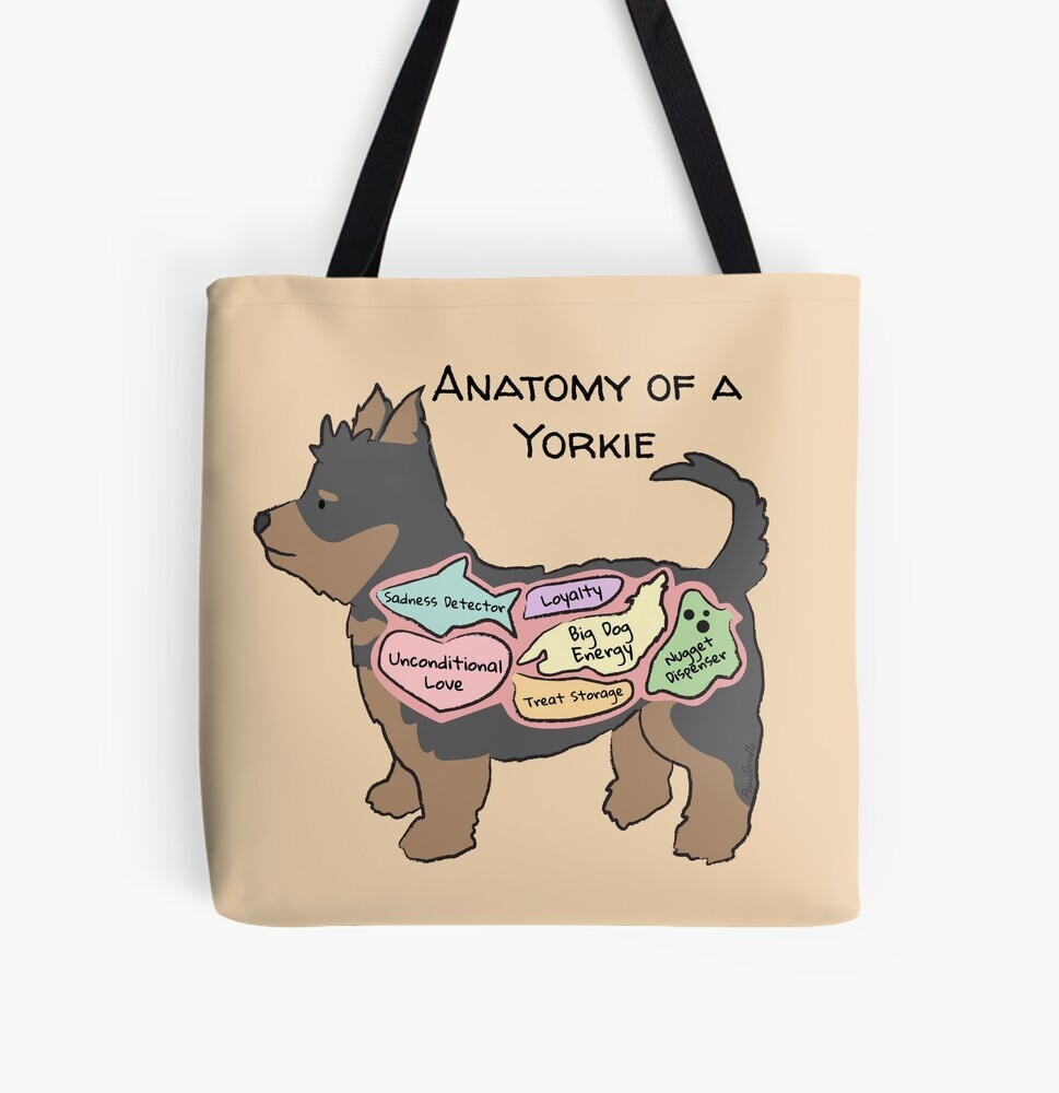 A beige-colored tote bag hanging off a wooden hook. On the tote bag features a cartoon illustration titled “Anatomy of a Yorkie” showing a cute Yorkshire Terrier dog with funny labeled anatomy sections.