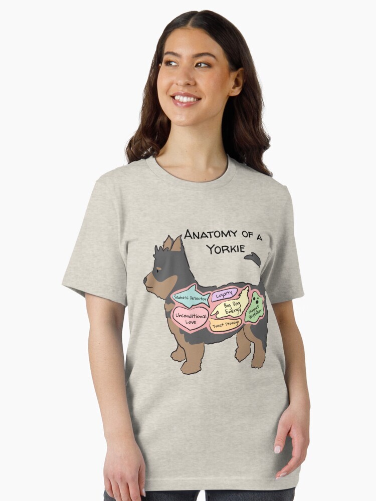 A brunette woman wearing a t-shirt  featuring a cartoon illustration titled “Anatomy of a Yorkie” showing a cute Yorkshire Terrier dog with funny labeled anatomy sections.